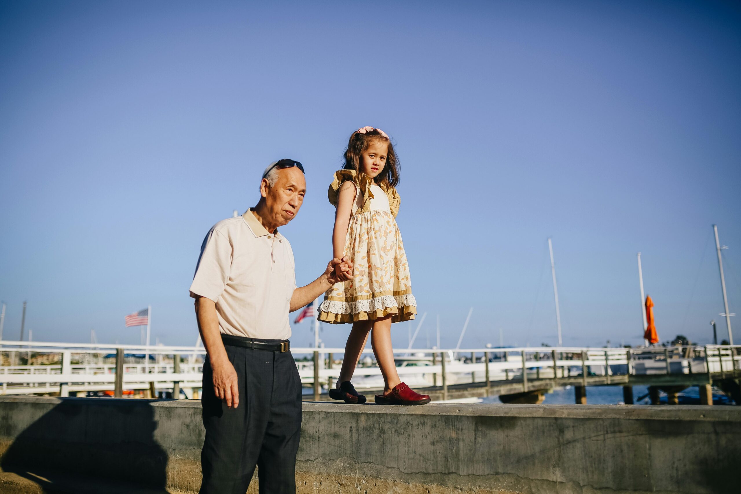 Charming moment of an elderly man and young girl holding hands and walking on a sunny pier.
