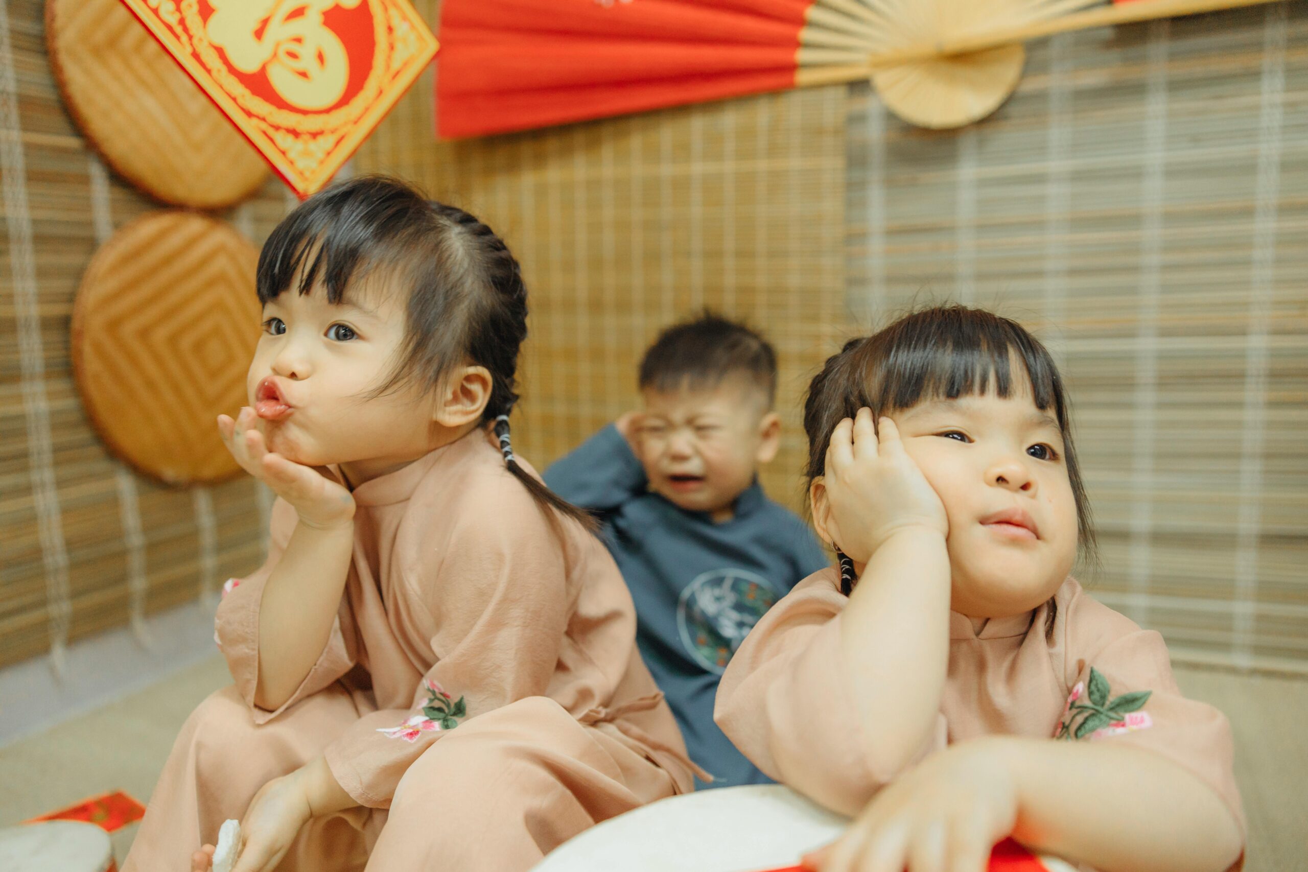 Cute Asian children in traditional wear, playful expressions indoors.